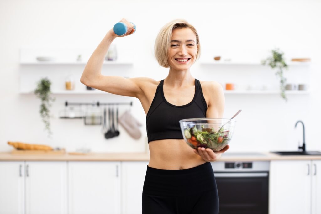 Smiling,Woman,Holding,Dumbbell,And,Bowl,Of,Healthy,Salad,In Sustainable diet
